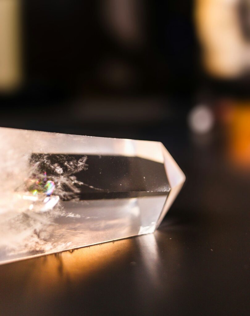 A clear quartz crystal point resting on a dark table in warm light